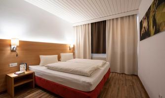A bright and modern bedroom with a double bed and wooden floor. The walls are in neutral colors and there is a window with curtains.