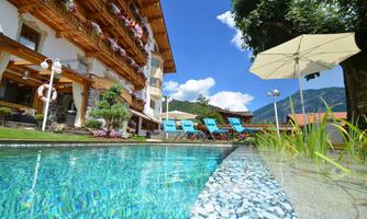 A beautiful pool area with cozy loungers and umbrellas. In the background, you can see an appealing building and a clear blue sky.