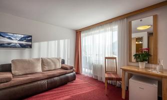 A cozy hotel room with a sofa, a table, and a television. Large windows provide plenty of daylight.