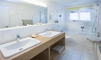 A modern bathroom with two sinks and a bathtub. Bright tiles and large windows create a friendly atmosphere.