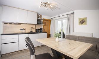 A modern kitchen with a large wooden table and a cozy sofa. Bright curtains let in plenty of light.