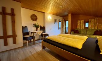 A cozy room with a double bed, a dining area, and a seating area. The wooden walls and ceilings create a warm atmosphere.