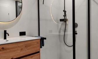 A modern bathroom with an elegant shower and a wooden sink. The decor is bright and designed in a minimalist style.
