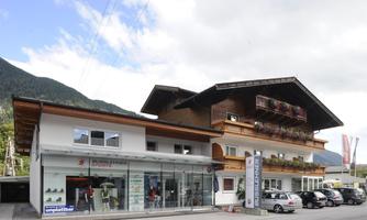 A modern office building with large windows and numerous cars in front of it. In the background, the mountains and a cloudy sky are visible.