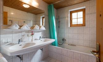 A modern bathroom with a bathtub and a shower. The room is bright and well-lit, with white tiles and a green shower curtain.