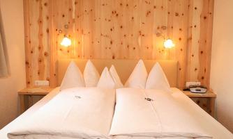 A cozy bedroom with a large double bed and several pillows. The walls are made of light wood, and there is soft lighting.