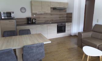 A modern kitchen with wooden cabinets and a dining area. The room is bright and inviting, featuring a cozy sofa.