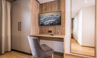 A modern room with a desk, a mirror, and a television on the wall. The warm wooden tones and stylish design create an inviting atmosphere.