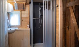 A simple bathroom with a shower and a sink. The walls are made of light wood and the light falls through a window.