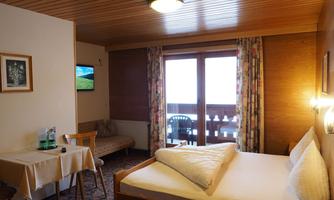 A cozy hotel room with a double bed and a small table. The balcony offers a view of the outdoors and the TV is mounted on the wall.