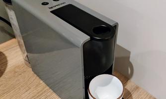 A modern coffee machine sits on a wooden table. A small cup is ready to receive fresh coffee.