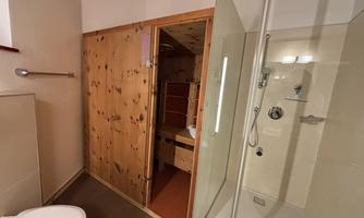 A modern bathroom with a glass shower and a wooden shelf. The walls are bright, and there is a toilet in the corner.