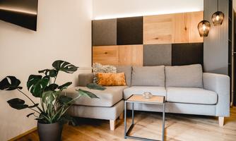 A modern living room with a gray couch and a small table. In the background, there is a decorative wall made of wood and fabric.