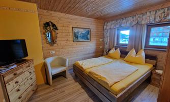 A cozy bedroom with wooden paneling. There are two beds, an armchair, and a television.