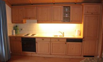 A modern kitchen made of wood with a bright working area. It is equipped with a stove, a sink, and kitchen cabinets.