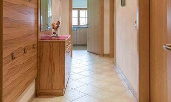 A bright hallway with tiled floor and wood paneling. Several coat hooks are hanging on the wall and there is a small table.