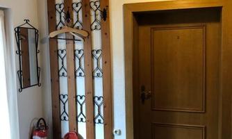 An entrance area with wood paneling, a door, and a coat stand. A fire extinguisher and a doormat are hanging on the wall.