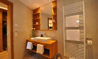 A modern bathroom with an elegant vanity combination and wooden shelves. It features large mirrors and a towel warmer.