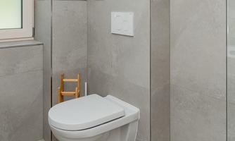 A modern bathroom with bright tiles and an elegant toilet. In the background, there is a glass shower wall and a small wooden bench.