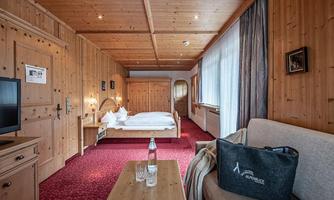 A cozy room with wood paneling and a red carpet. It is furnished with a double bed, a sofa, and a small seating area.