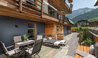 A modern terrace with garden furniture and loungers. In the background, mountains and other buildings can be seen.