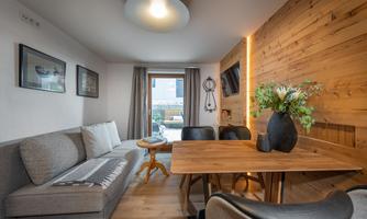 A modern furnished living space with a gray sofa and a wooden table. Large windows provide plenty of natural light and an inviting atmosphere.