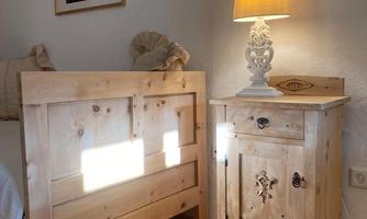 A cozy bedroom with a wooden bed and a nightstand. A lamp provides warm light and a picture hangs on the wall.