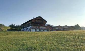 A traditional building in the mountains, surrounded by green meadows. The sky is clear and blue.