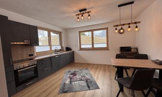 A modern kitchen with wooden and black cabinets. A dining area with a table and chairs creates an inviting atmosphere.