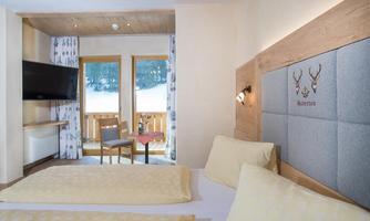 A cozy bedroom with two beds and modern furniture. Large windows offer a view of the snowy landscape outside.