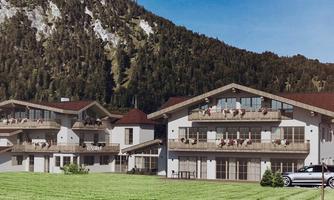 A hotel building in a picturesque mountain landscape. The façade is modern, with balconies and adjacent green meadow.
