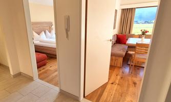 A well-designed room with two doors. On the left side is a bedroom and on the right side a cozy dining area with a wooden chair and table.