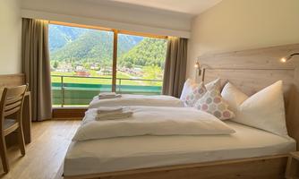 A cozy bedroom with two beds and a large window that offers a view of the mountains. The furnishings are modern and bright.