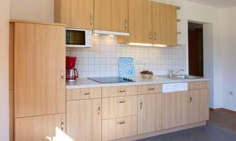A modern kitchen with wooden cabinets and a bright countertop. There is a microwave, a coffee machine, and plenty of storage space.