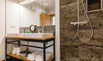 A modern bathroom with a shower and a wooden vanity. The walls are painted in neutral tones and there are towels on a shelf.