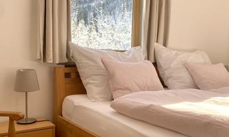 A cozy bedroom with a large bed and many pillows. Through the window, one can see snow-covered mountains.