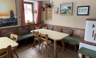 A cozy interior with wooden tables and chairs. Pictures hang on the wall, and there is a fireplace in the corner.