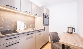 A modern kitchen with gray cabinets and a minimalist design. There is a dining area with a table and a chair.