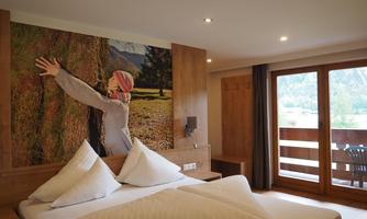 A cozy hotel room with two beds and a wooden wall. On the wall hangs a large picture of a person hugging a tree.