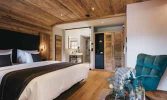 A modern bedroom with wood paneling and a large bed. Next to the bed is a comfortable armchair and a small table with a plant.