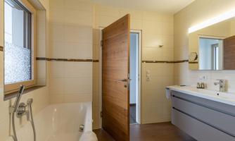 A modern bathroom with a bathtub and a double sink. The walls are brightly tiled and there is an open door to another room.