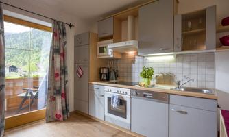 A modern kitchen with wooden floors and large windows. The decor is bright and functional, with a beautiful view of the mountains.