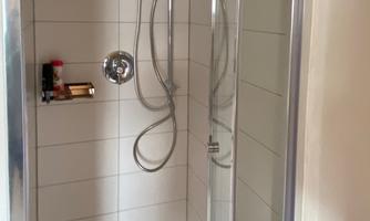A small shower cubicle with glass walls and modern fixtures. The walls are light tiled and the shower fittings are elegant.