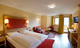 A cozy hotel room with a double bed and a red sofa. Large windows provide plenty of daylight and a view outside.