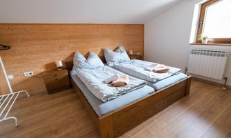 A cozy bedroom with two single beds and wooden paneling. The room has a window and modern heating.