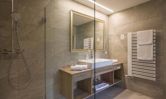A modern bathroom with a glass shower and an elegant sink. The walls are clad in natural stone, and there are bright towels as well as a large mirror.
