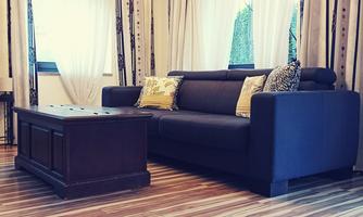 A modern living room with a dark blue sofa and a wooden table. Curtains and a light floor create an inviting atmosphere.
