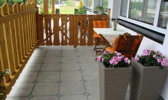 A cozy balcony with a wooden railing and orange chairs. Two large planters with colorful flowers are decoratively placed.