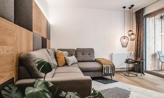 A modern living room with a comfortable gray sofa and stylish hanging lamps. Large windows provide plenty of daylight and a view outside.