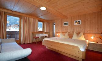 A cozy wooden hotel room with a double bed and a sofa. A view of the mountains is visible through the window.